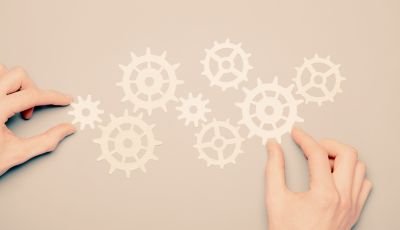 Hands arranging white gear shapes on a beige background