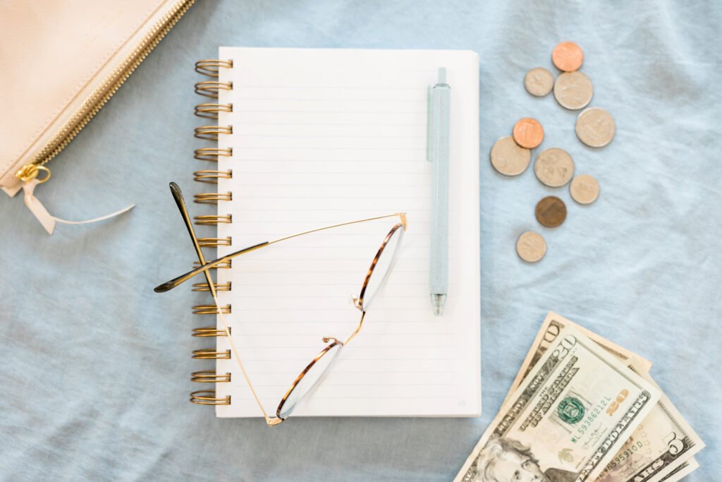 Notebook, glasses, coins and cash arranged on a desk
