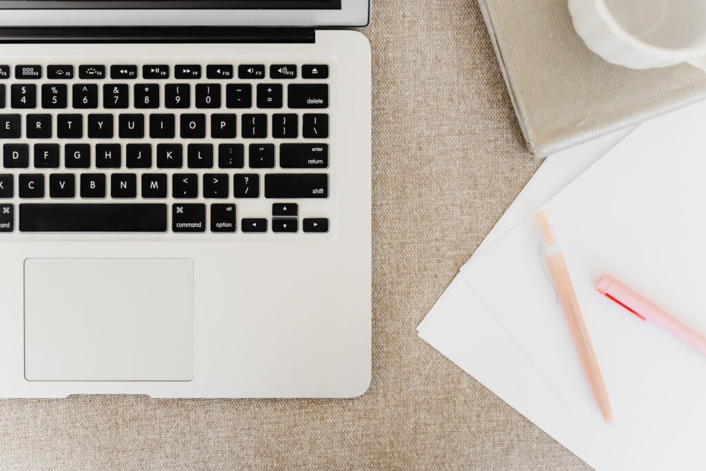 Laptop, notebook and pens arranged on a neutral office desk