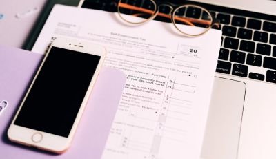 Laptop, smartphone, glasses and paperwork arranged on a desk