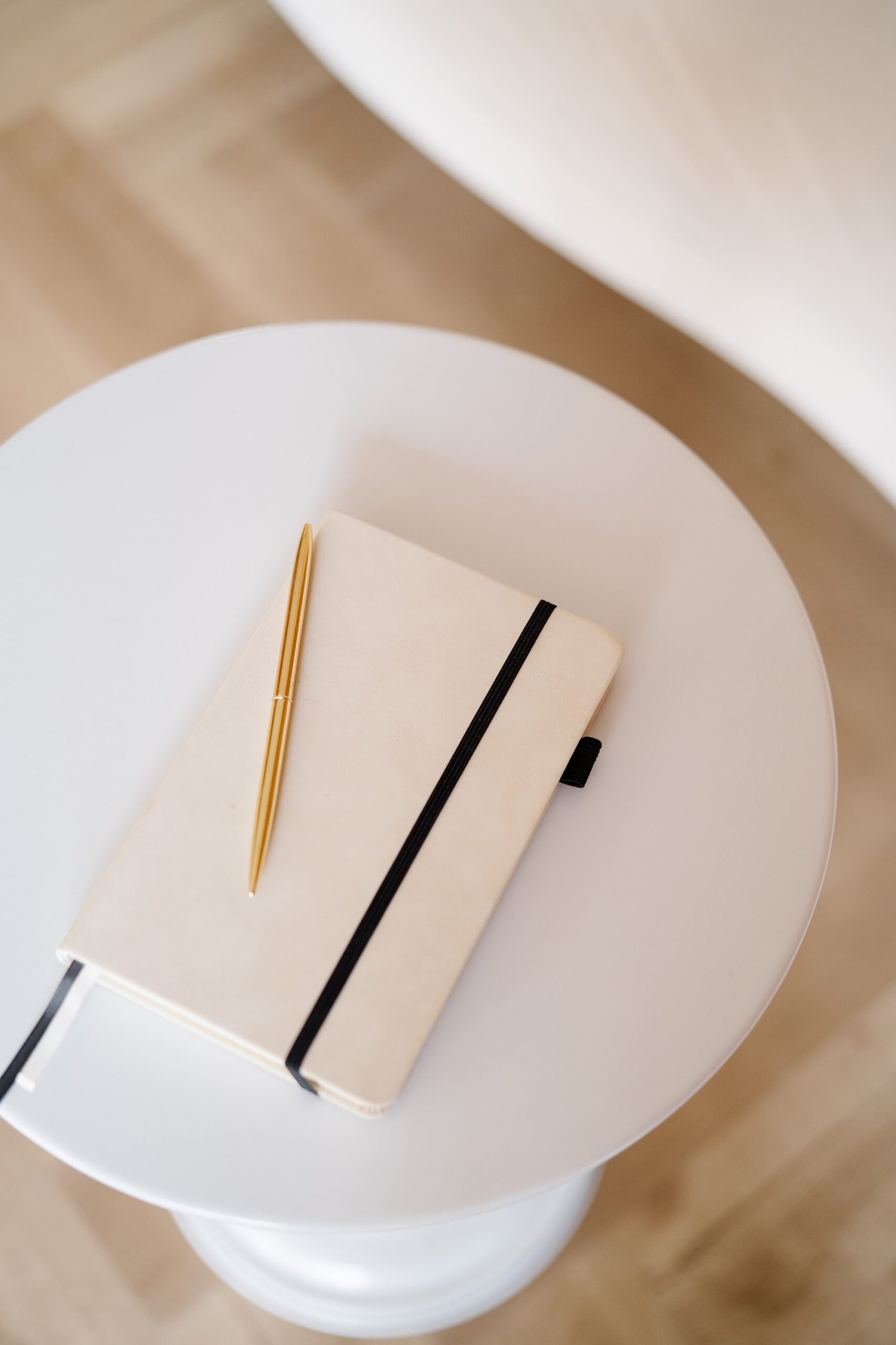 Cream notebook with gold pen on a white side table