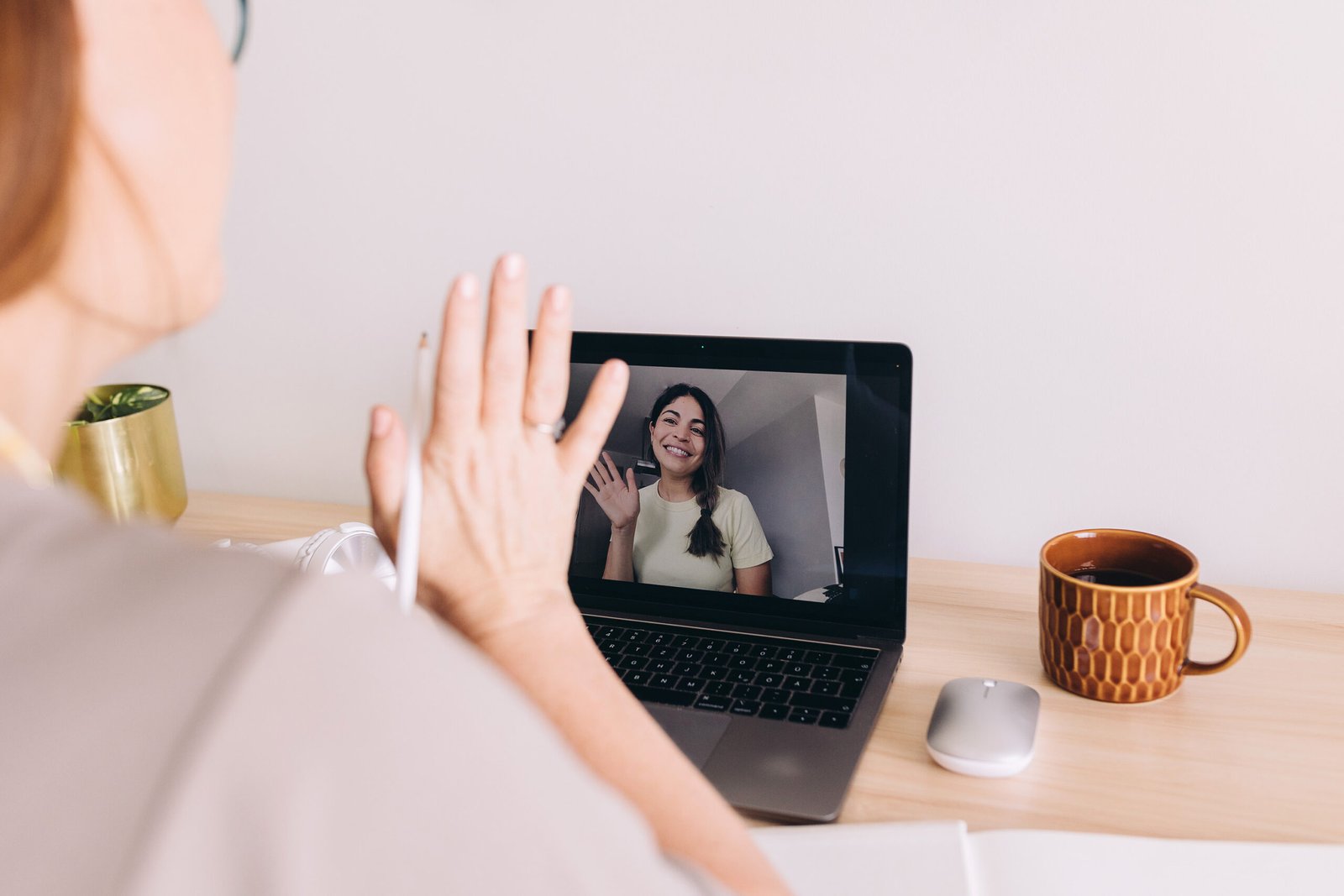 Woman waving during a video call on a laptop at a home office desk